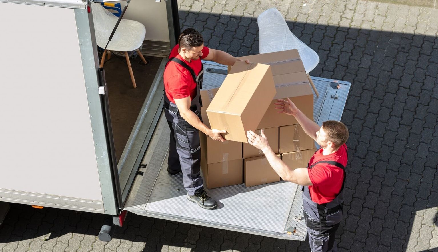 Zwei Arbeiter übergeben eine Kiste auf der LKW Ladezone